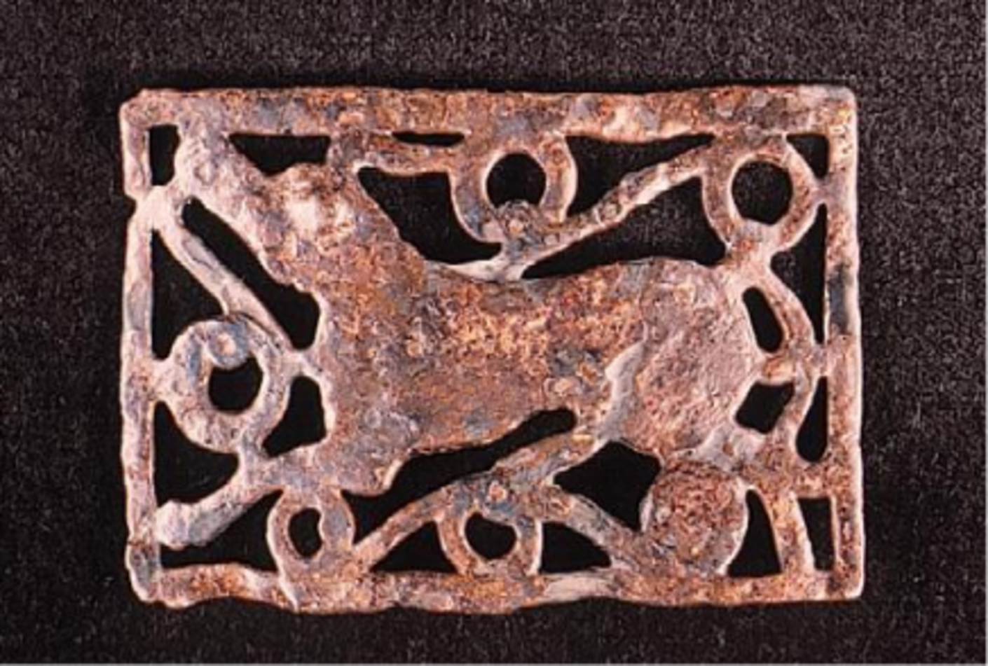 Objet archéologique en métal, représentant un animal stylisé entouré de motifs géométriques, probablement une boucle de ceinture ou un élément décoratif