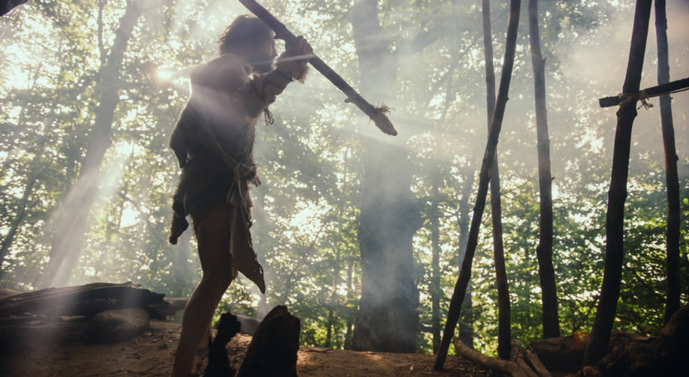 Reconstitution paléolithique : une personne vêtue d'une tenue ancienne, tenant une lance, dans une forêt baignée de lumière matinale