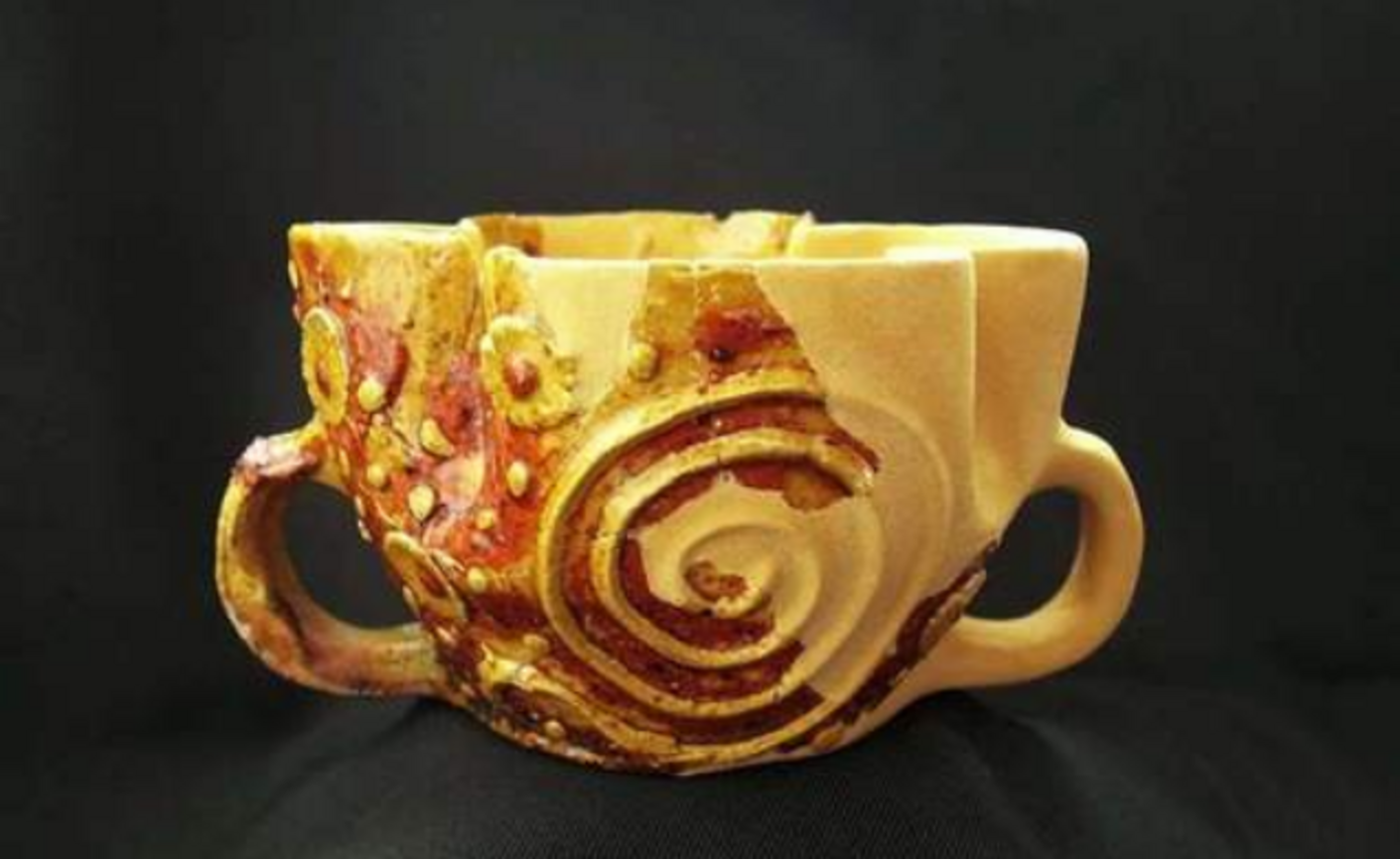 Vase ancien décoré de motifs en relief représentant des volutes et des anses latérales, typique de l'artisanat du moyen âge classique.